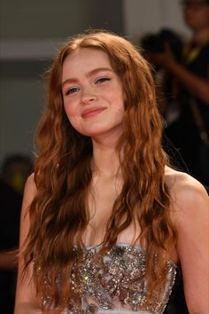 a woman with long red hair standing in front of a camera