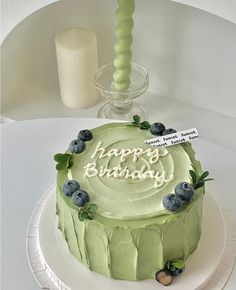 a green birthday cake sitting on top of a white plate next to a glass vase