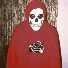 a skeleton in a red cloak holding a donut