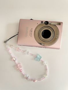 a pink camera sitting on top of a white table next to a beaded necklace