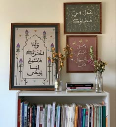 there are two framed pictures on the wall above a bookshelf with flowers in vases