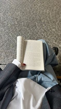 an open book sitting on top of a bed next to a pair of jeans and tie