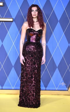 a woman with red hair wearing a purple dress and standing in front of a blue wall