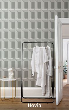 an open closet with clothes on hangers next to a white chair and wallpaper