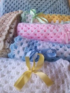 four crocheted blankets with yellow ribbon on top and blue, pink, white, and beige colors