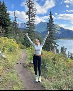 a woman is standing on a trail with her arms in the air