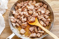 meat and spices cooking in a skillet with a wooden spoon next to it on a table