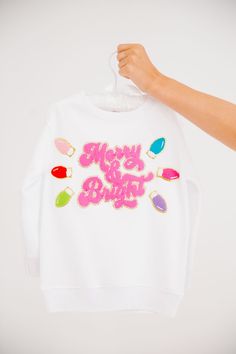 Get your little ones in the festive spirit with our MINI KIDS MERRY & BRIGHT WHITE PULLOVER. This white pullover features a playful pink Merry & Bright patch and festive christmas lights patches. Perfect for adding a touch of holiday cheer to their outfit! All orders are currently shipping within 14 business days. To receive item quicker, expedited shipping is available at checkout. **All Christmas orders must be placed with expedited shipping to guarantee delivery by Dec. 24 if placed after Dec White Festive Holiday Sweater, White Holiday Festive Sweater, Cute White Holiday Tops, Fun White Holiday Tops, Cute White Top For Festive Occasions, Playful White Winter Top, Playful White Tops For Winter, Cute White Christmas Sweatshirt, Fun White Winter Tops