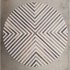 a round wooden table sitting on top of a cement floor next to a white and brown striped wall