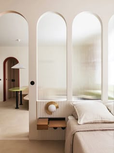 a bed sitting under three arched windows next to a table with a lamp on it