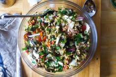 a glass bowl filled with salad on top of a wooden cutting board next to bowls of vegetables