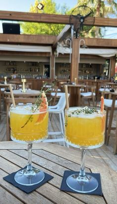 two glasses filled with drinks sitting on top of a wooden table next to each other