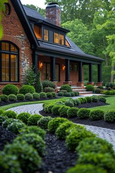 a brick house surrounded by lush green trees and bushes in front of it is lit up at night