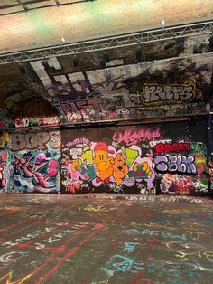 an empty parking garage with graffiti all over the walls and floor, under a bridge