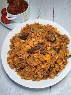 a white plate topped with rice and meat next to a bowl of chili sauce on a table