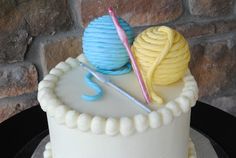 there is a white cake with blue and yellow icing on the top it has two crochet hooks