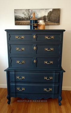 a blue dresser with gold handles in a room next to a painting on the wall