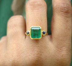 a person's hand with a ring on it and a green stone in the middle