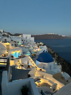 the white buildings are lit up at night by the water's edge with blue domes