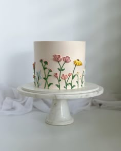 a white cake with pink and yellow flowers painted on the top is sitting on a pedestal