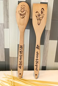 two wooden spoons with cartoon faces on them next to some spaghetti noodles in front of a striped wall