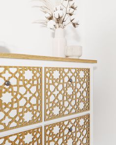 a white vase with flowers on top of a wooden dresser next to a wall mounted mirror