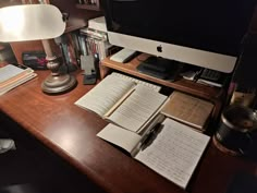 an apple computer sitting on top of a wooden desk next to a lamp and books