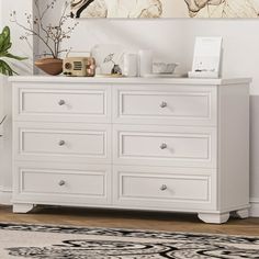 a white dresser sitting in a room next to a plant and pictures on the wall