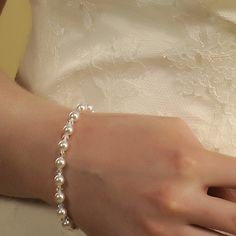 a close up of a person wearing a wedding dress and holding a bracelet with pearls on it