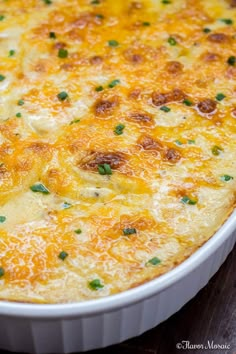 a cheesy casserole in a white dish on a wooden table with green garnish