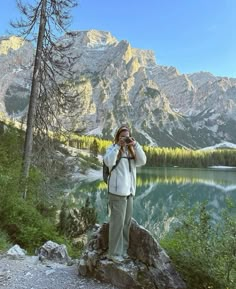 a person standing on top of a rock next to a lake with mountains in the background