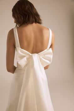 the back of a woman wearing a white dress with a large bow on it's shoulder