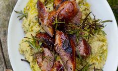 some meats and rice on a white plate with green garnish, sitting on a wooden table