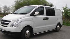 a white van parked on the side of a road next to some grass and trees