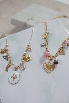 This charm necklace is so sweet and perfect, we can't even handle it. Features mostly vintage mixed-metal charms, hanging on pearls and sterling silver curb chain - to give it just a touch of edginess. 7 charms hang from a strand of sterling freshwater pearls, with a pinkish hue: gold plated vintage teddy bear stainless vintage western hat gold plated cowgirl boot enameled, hand-painted rose charm from the 1960s in center silver plated vintage angel charm gold plated vintage butterfly charm enam Charm Necklace Custom, Vintage Style Metal Necklaces With Charms, Dainty Metal Necklaces With Vintage Charm, Vintage Metal Charm Necklace, Whimsical Pearl Charm Jewelry As Gift, Whimsical Pearl Charm Jewelry For Gifts, Whimsical Pendant Necklace With Vintage Charm, Whimsical Vintage Charm Pendant Necklace, Gold Necklaces With Dangling Charms For Vintage Collection