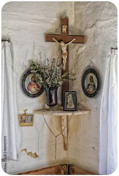 a cross on the wall above a table with pictures and flowers in front of it