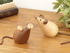 two wooden mouses sitting on top of a table next to some books and a potted plant