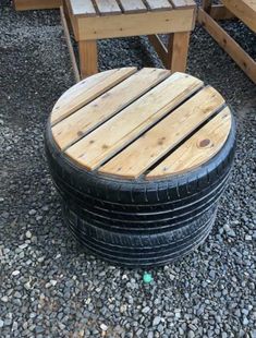 several wooden tables and chairs made out of old tires are sitting on graveled ground