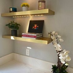 two shelves with flowers and books on them in a corner next to a wall light