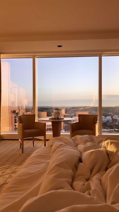 a large bed sitting next to two chairs in front of a window filled with lots of windows