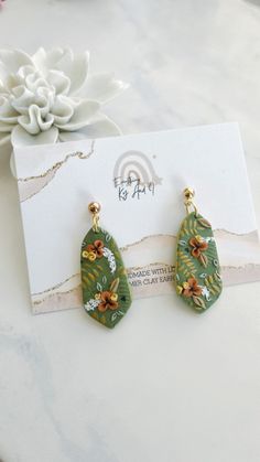 the earrings are green and yellow with flowers on them, sitting next to a card