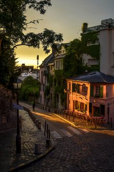 the sun is setting on an old street with tables and chairs in front of buildings