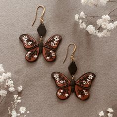 two brown and white butterfly shaped earrings sitting on top of a table next to flowers