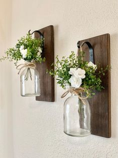 two mason jars with flowers are hanging on the wall