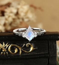 a white diamond ring sitting on top of a wooden table next to a vase with flowers