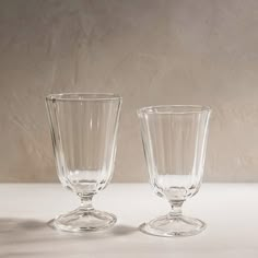 two clear glass goblets sitting side by side on a white tableclothed surface