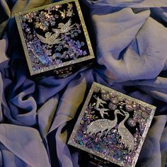 two decorative boxes sitting on top of a blue cloth