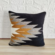 a black and yellow pillow sitting on top of a wooden floor next to a white brick wall