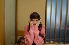 a young woman sitting at a desk with her hands on her face and looking up