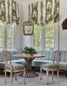 a living room with two couches and a table in front of three large windows